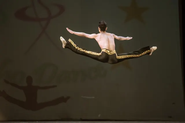 Bailarín adulto con pantalón negro y dorado en un salto extendido durante EDC 2019.